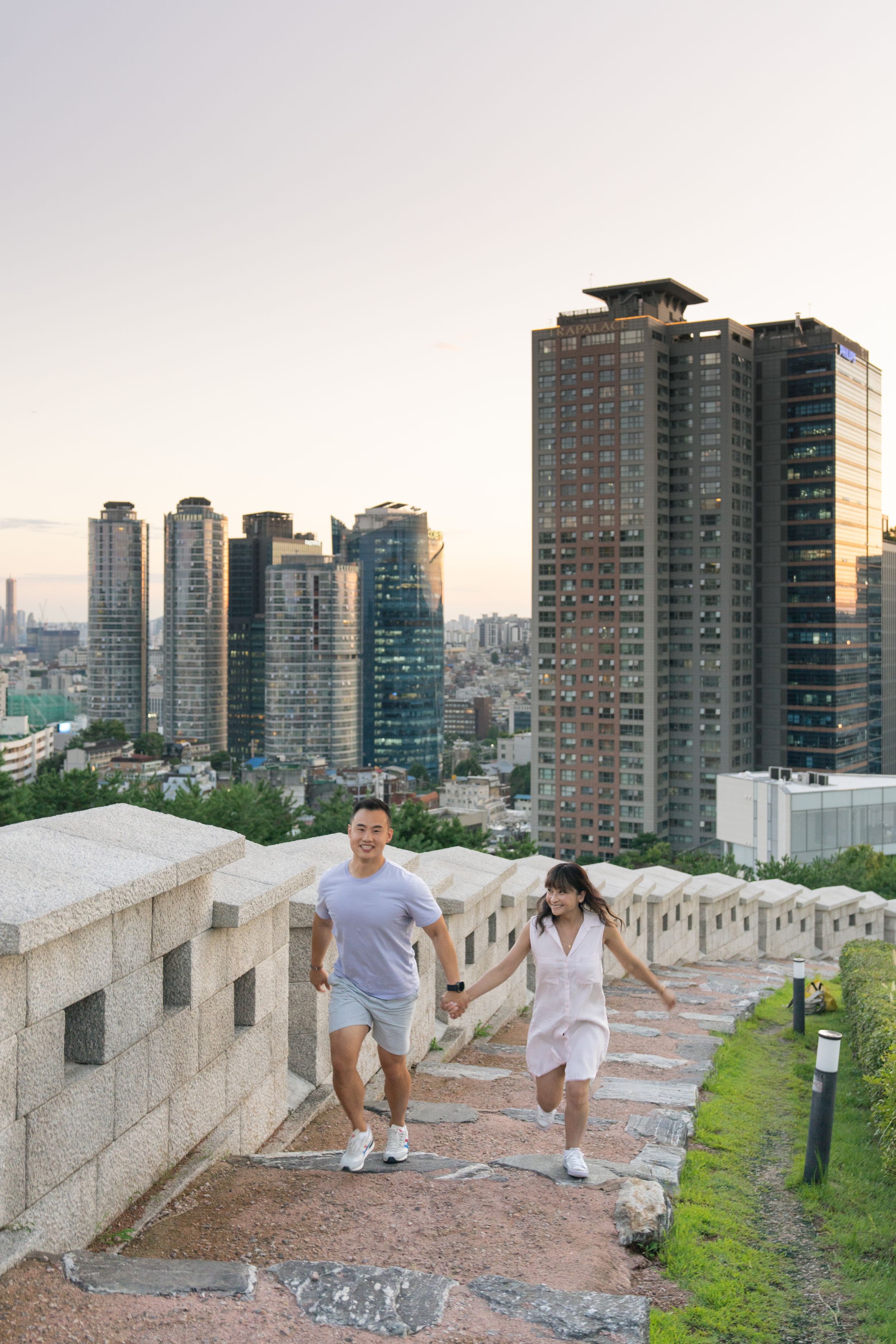 A group of people exploring a historic city wall with modern high-rise buildings visible in the background at sunset.