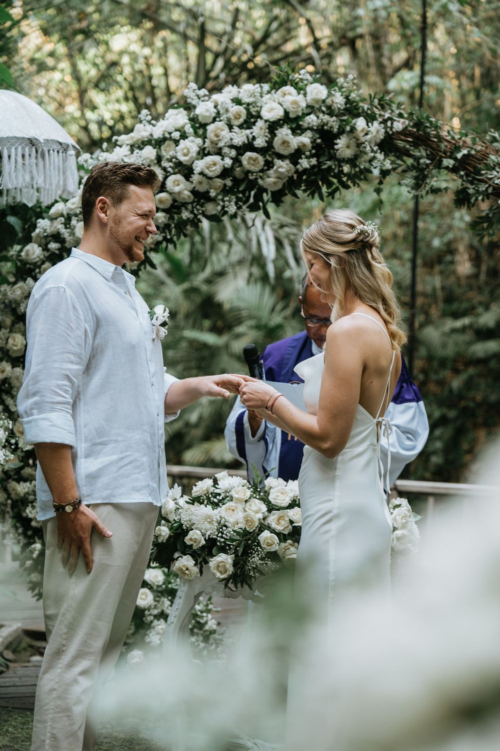 Romantic wedding ceremony under a floral arch with white roses in a garden setting.