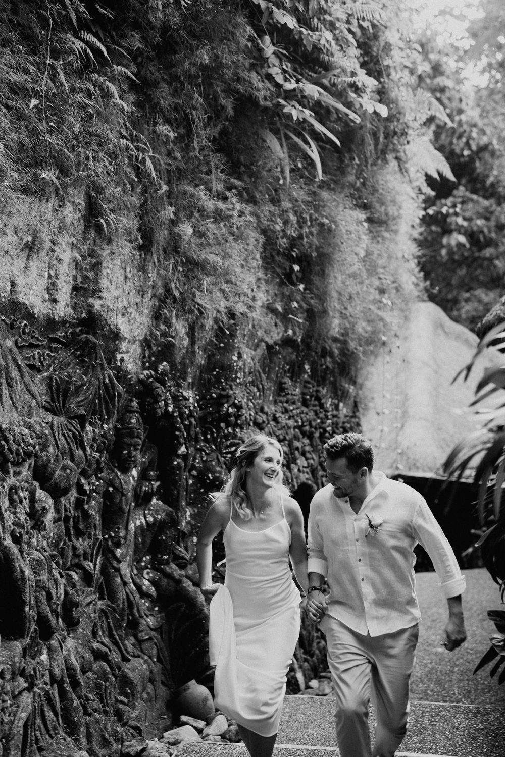 Black and white photo of a couple walking along a scenic pathway surrounded by lush foliage.
