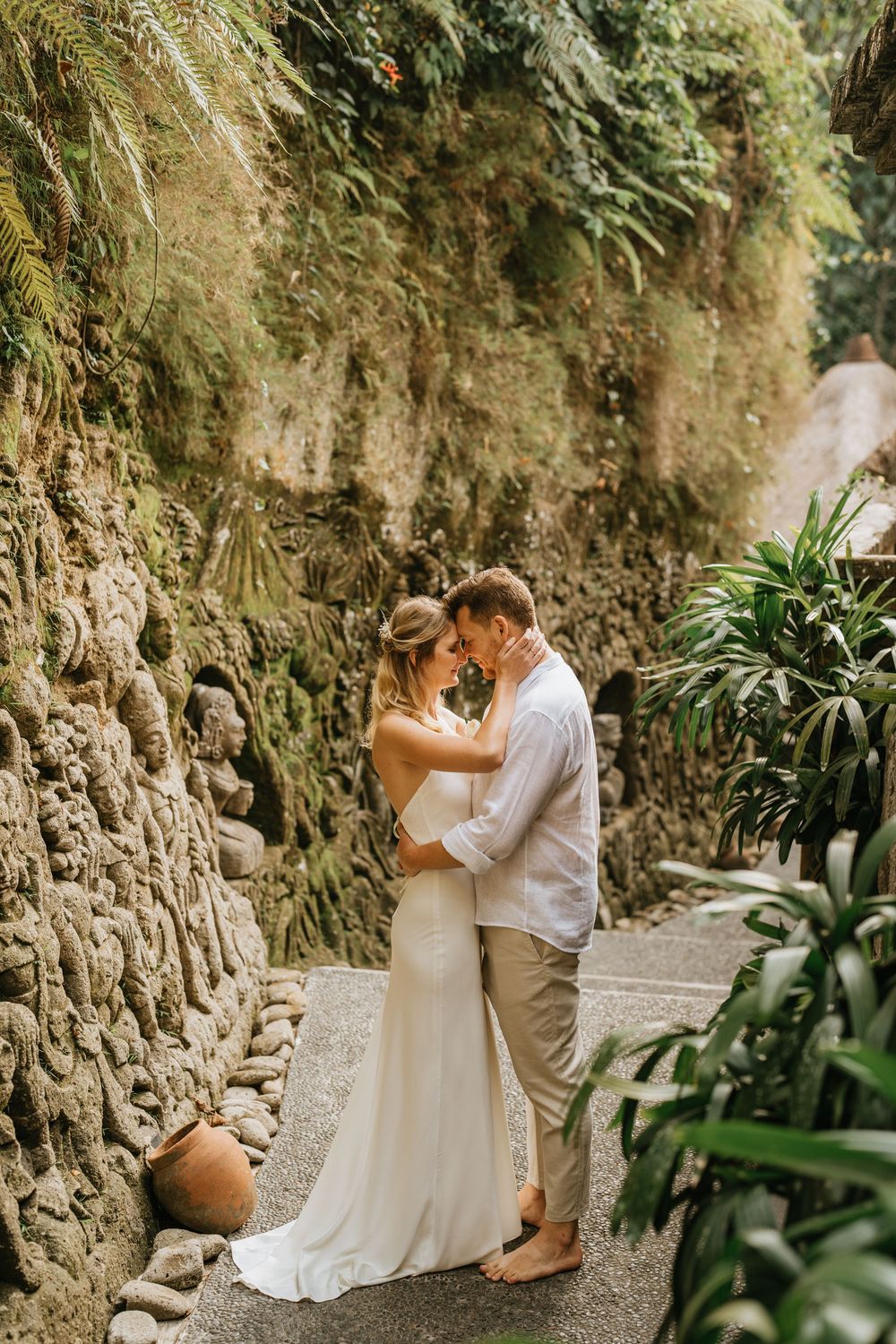 Intimate wedding moment against a rustic stone wall with tropical plants.