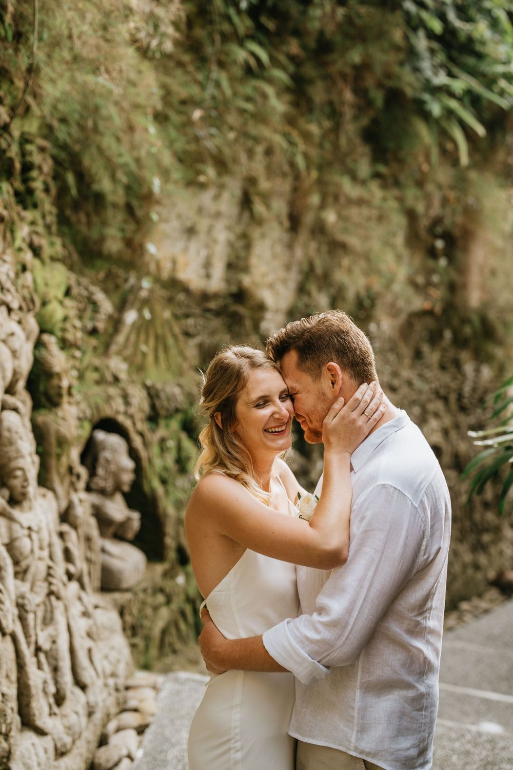 Tender wedding moment captured against natural stone wall and greenery.