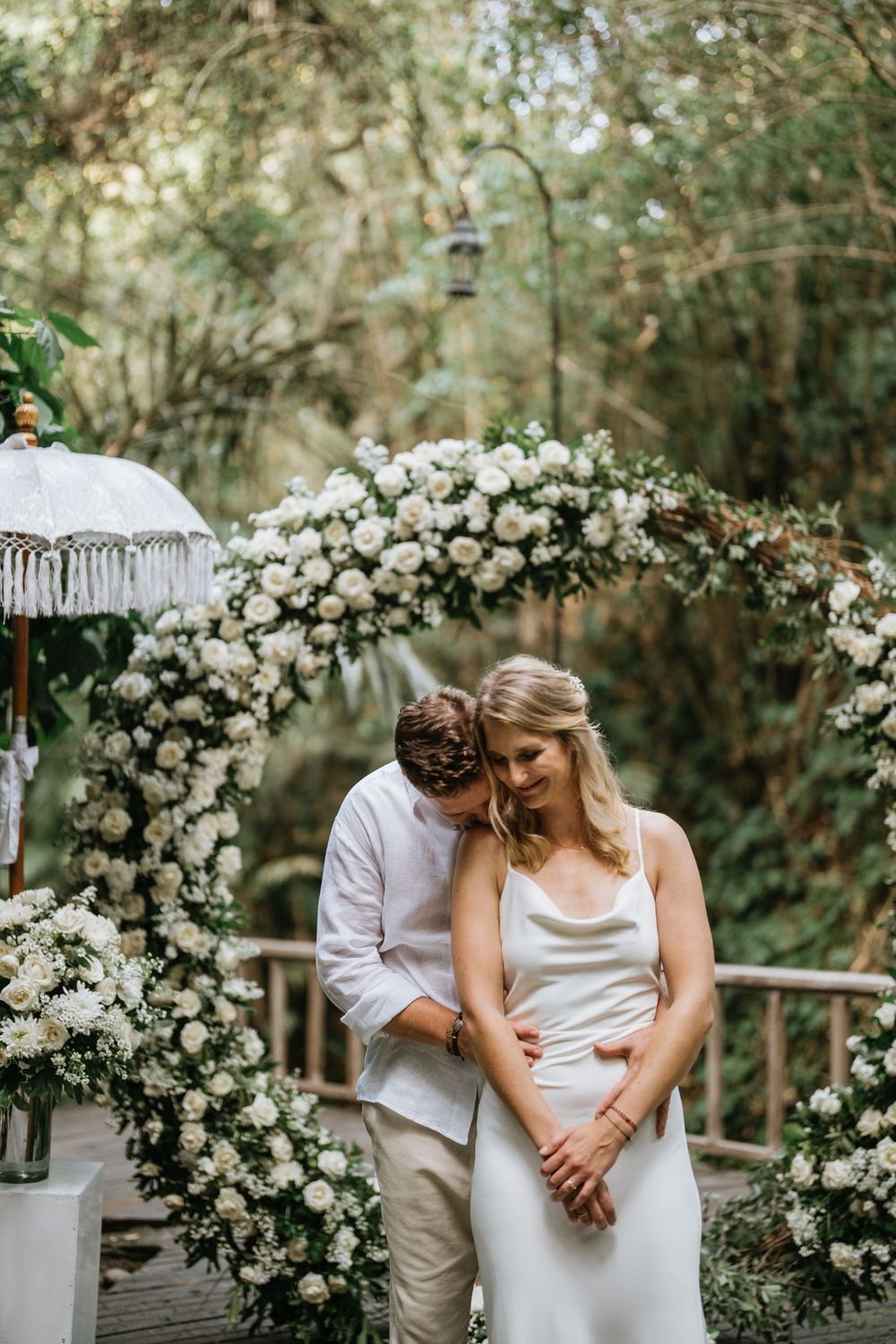 Wedding portraits under a white rose floral arch in a garden setting.
