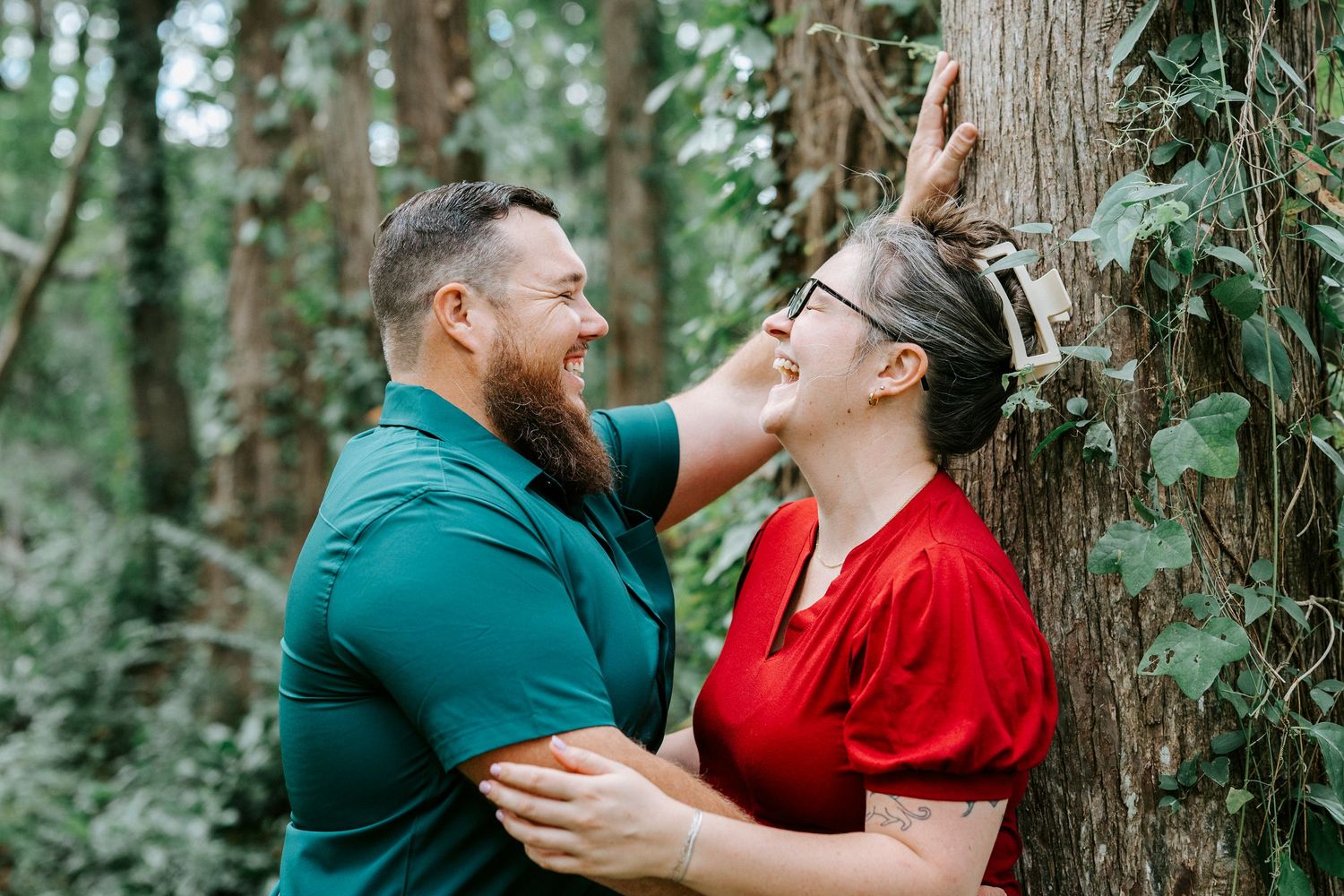 Romantic forest photoshoot with couple among trees wearing red and green outfits.