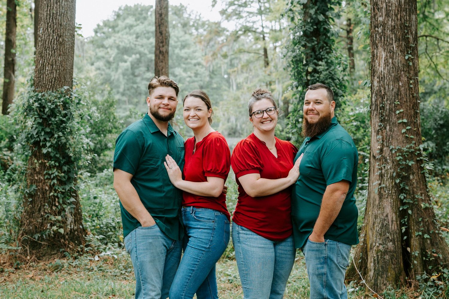 A group of people poses in a wooded outdoor setting wearing coordinated casual outfits in red and dark green tones.