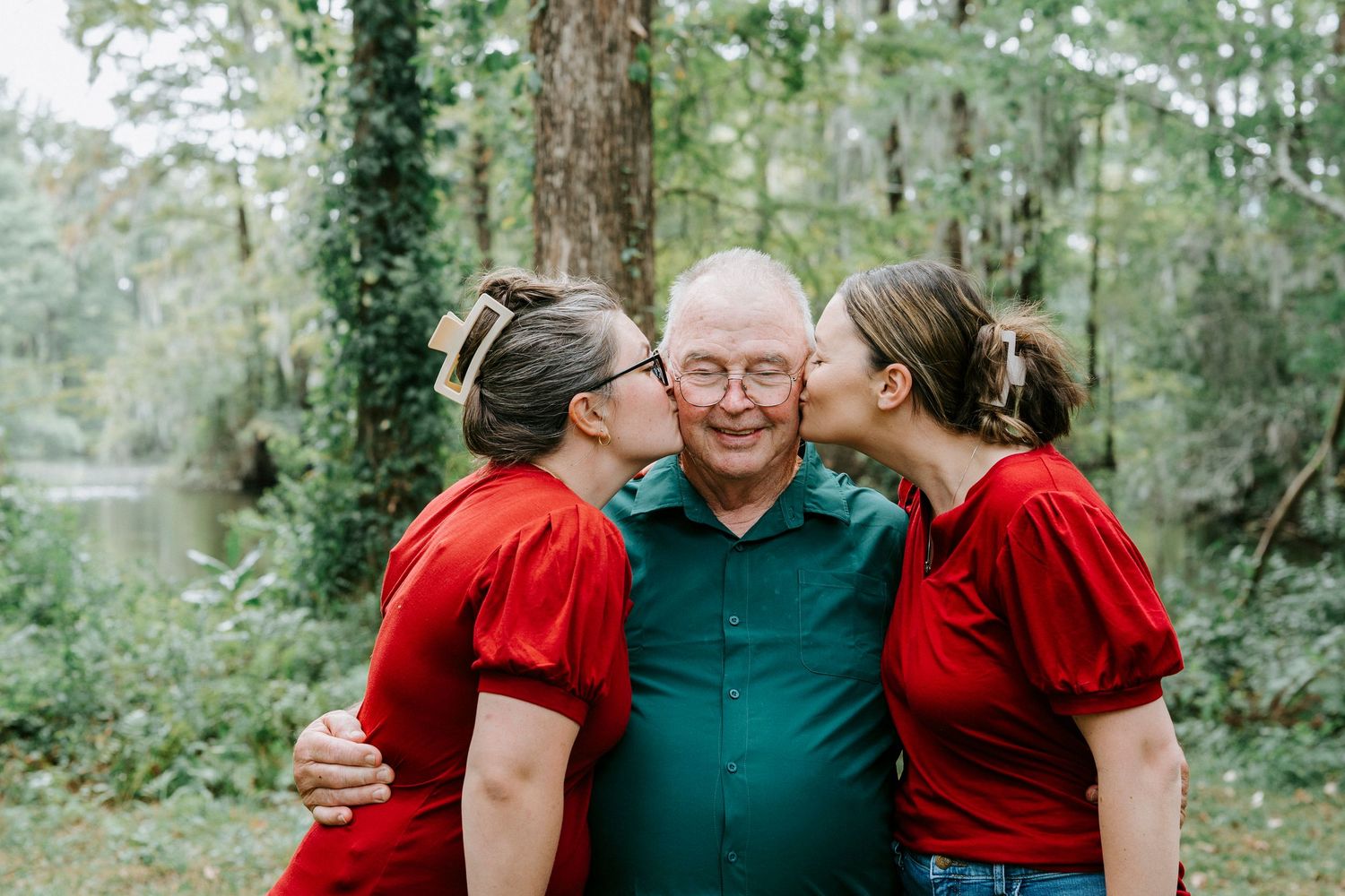 People wearing coordinated red and teal outfits pose outdoors together in a wooded setting for family photos.