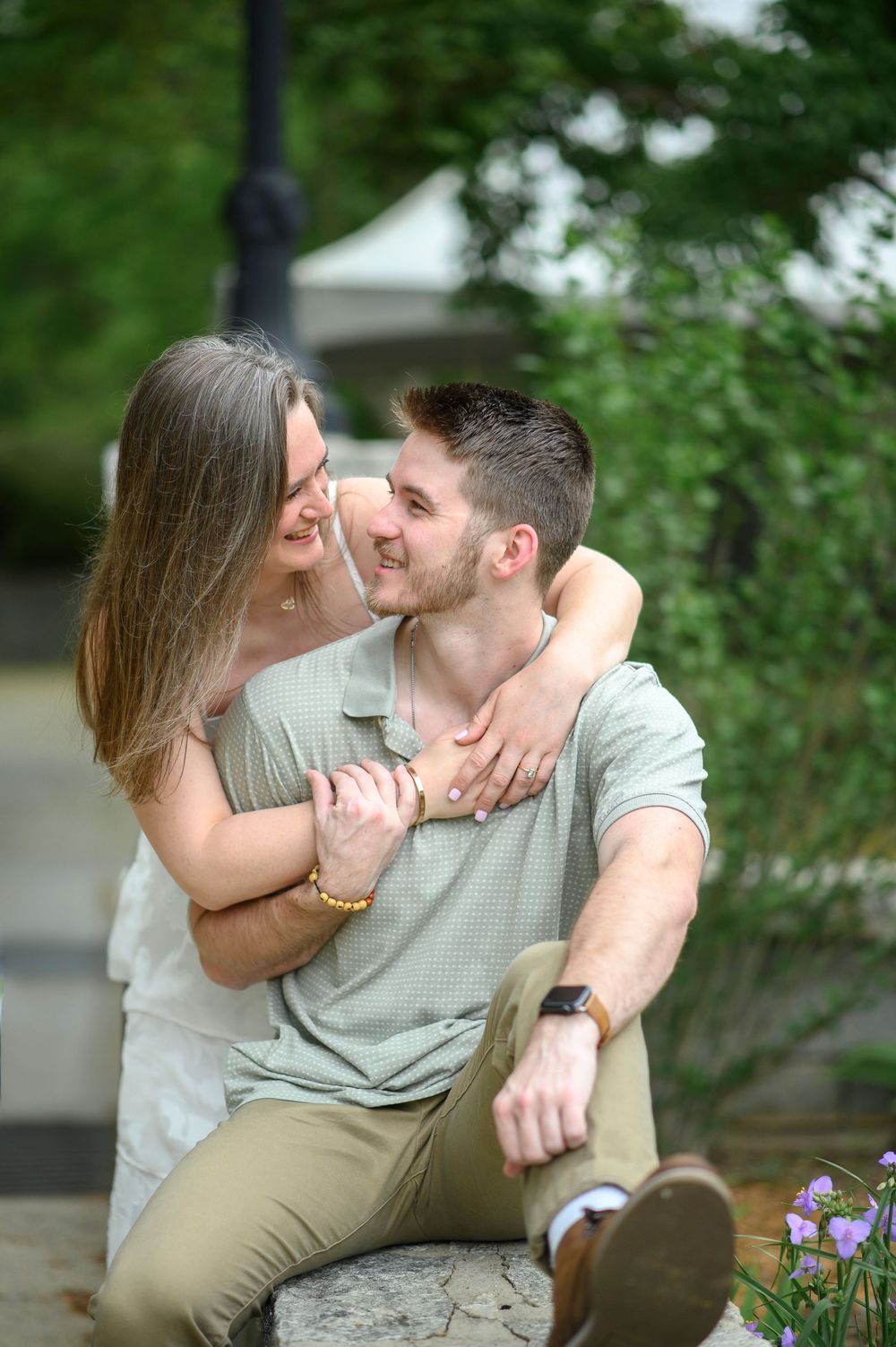 A romantic couple shares an intimate kiss while sitting on a park bench surrounded by greenery.