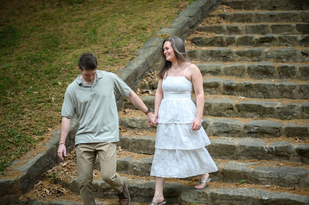 A couple in casual attire takes candid photographs on stone steps in a garden setting.