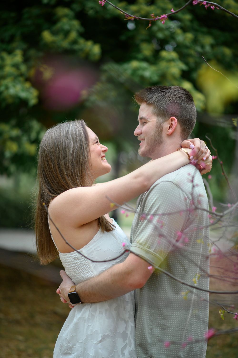 Romantic couple sharing intimate moments in a garden setting with greenery and pink flowers.
