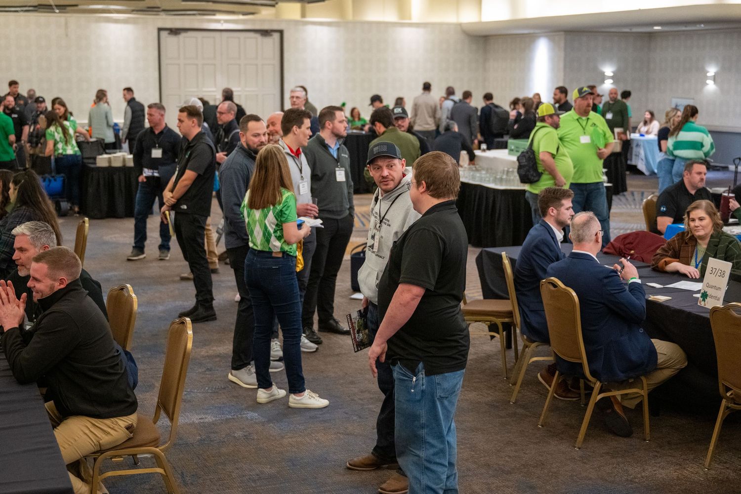 People gathered in a large conference room participate in various group activities and discussions at rectangular tables.