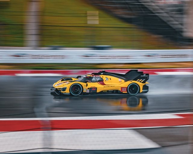 Yellow race car speeding on a wet track with motion blur.
