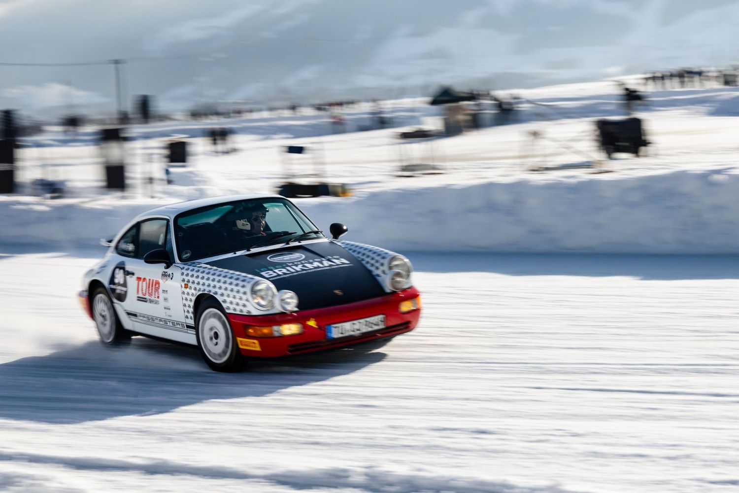Classic cars racing on a snowy winter track during a motorsport event.