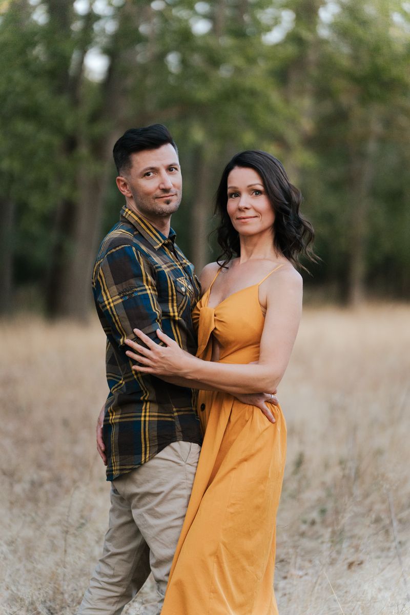 Couple in a plaid shirt and yellow dress embrace in a dreamy autumn field while dancing together in a photoshoot in Sydney
