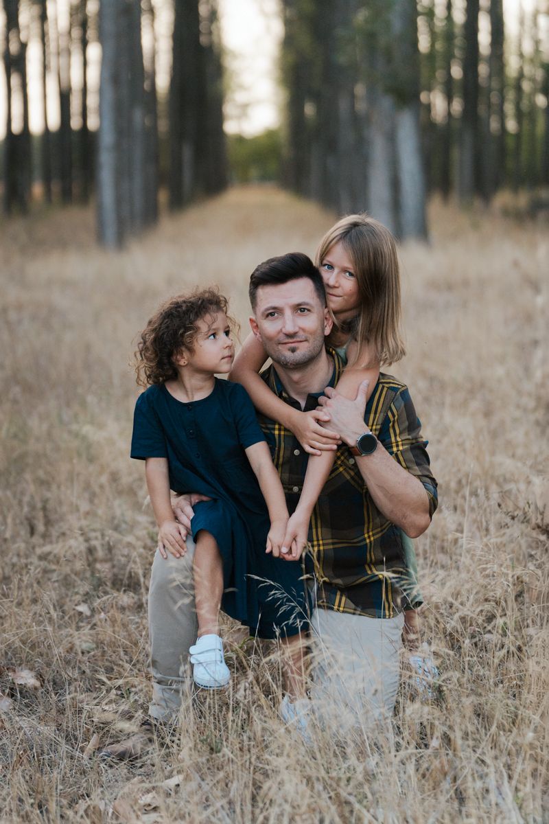 A family sitting together in a field of tall grass near trees during golden hour family photoshoot western sydney