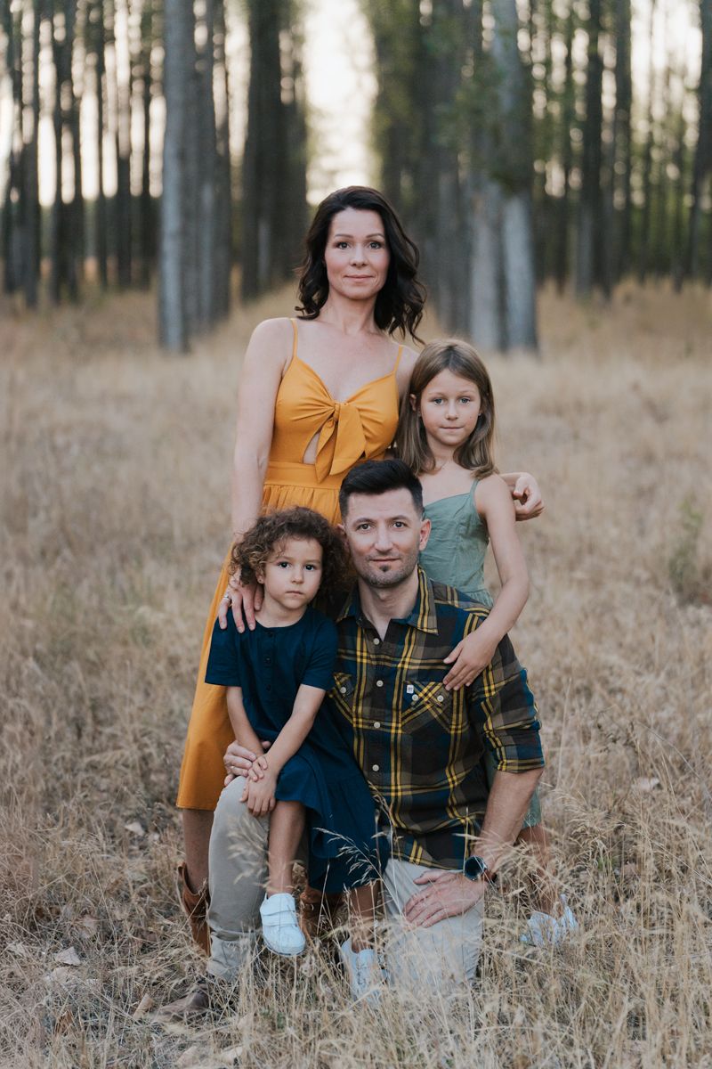 Family poses together in a forest setting with tall trees and golden grass at sunset during a  western sydney photoshoot