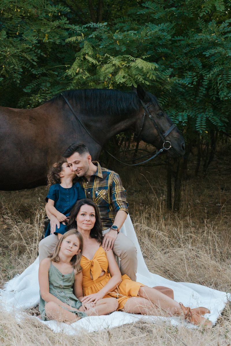 Family and horse lay together on a blanket in a grassy field surrounded by green trees in Western Sydney Family photoshoot with a horse