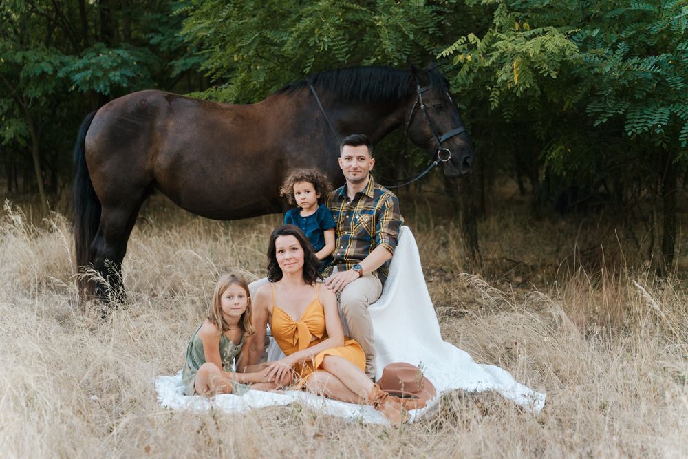 Group relaxes on a white blanket with a horse in a rustic outdoor setting at sunset during a family photoshoot in western sydney