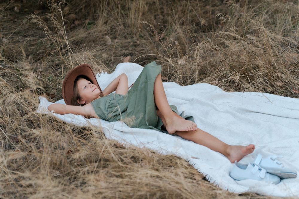 girl lounging on white blankets in a sun-dappled field with a horse nearby during a family photoshoot in Western Sydney Parklands