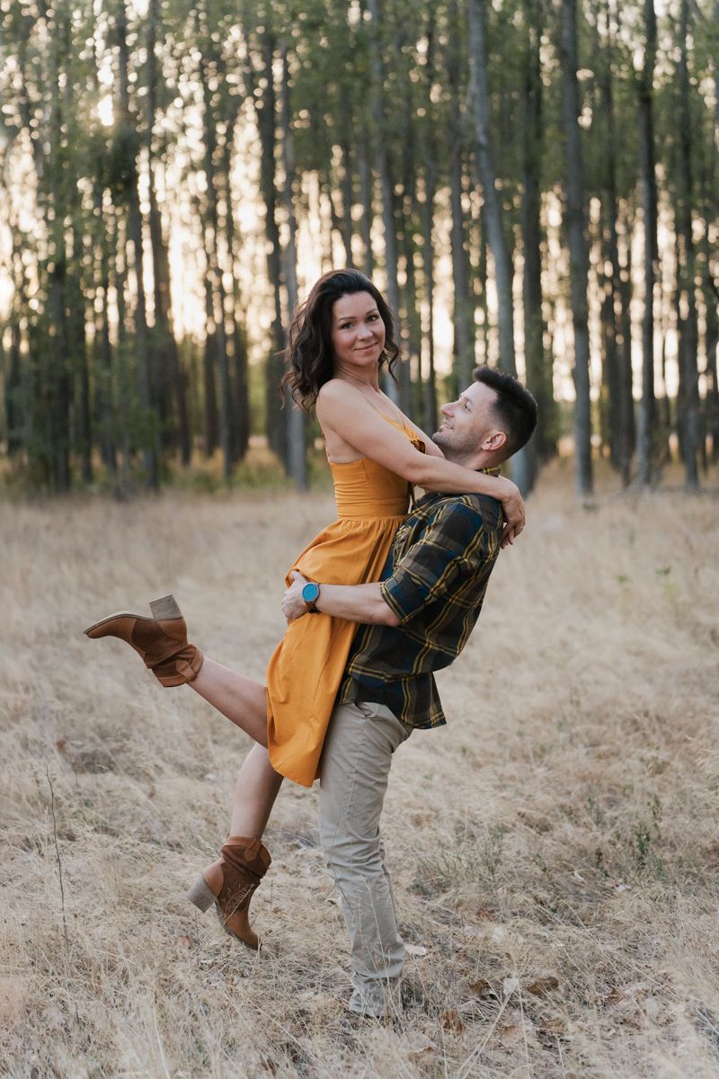 A romantic couple in a yellow dress and casual wear embrace joyfully in a sun-dappled forest setting in western sydney parklands photoshoot