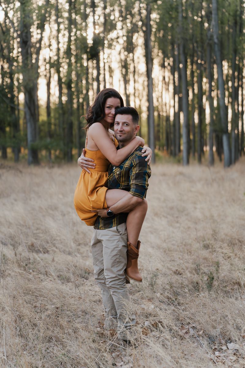 A couple embraces playfully in a golden field surrounded by tall trees during sunset couples photoshoot in Western Sydney