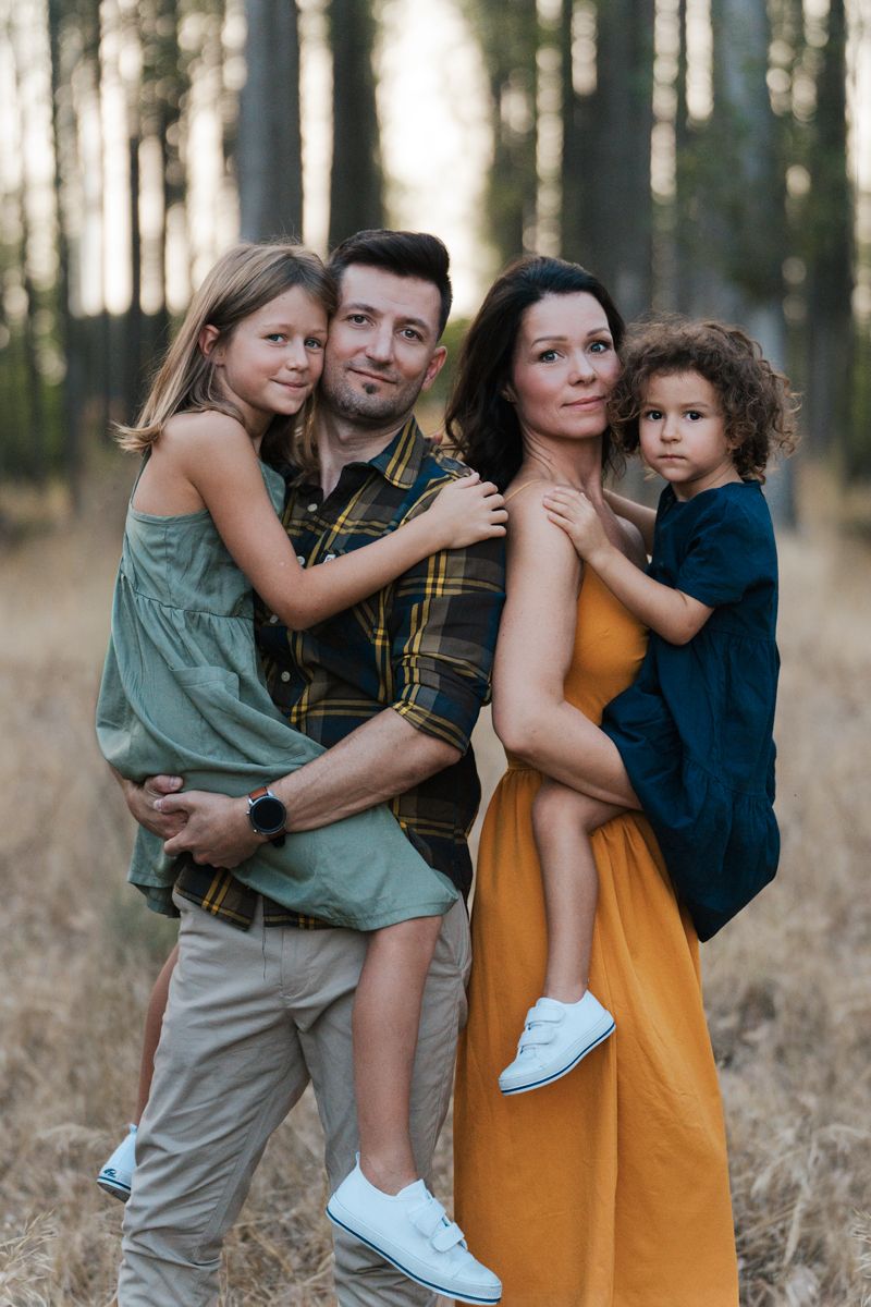 A family of four poses together in a forest setting, wearing casual clothing in earthy tones in western Sydney Parklands family photoshoot