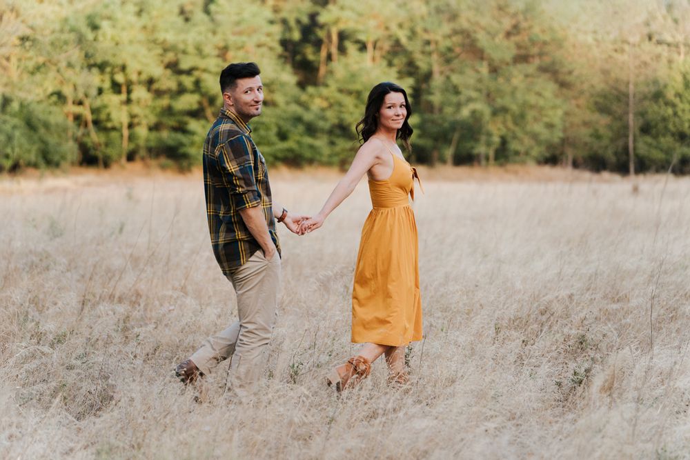 A couple walks together through tall golden grass while holding hands during an autumn sunset photoshoot in Sydney