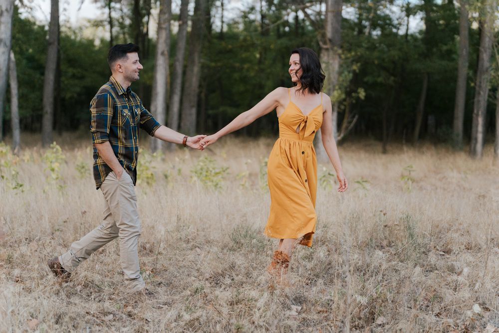 Woman in a yellow dress and man in blue stands in a dried grass field during autumn with trees in the background western sydney parklands