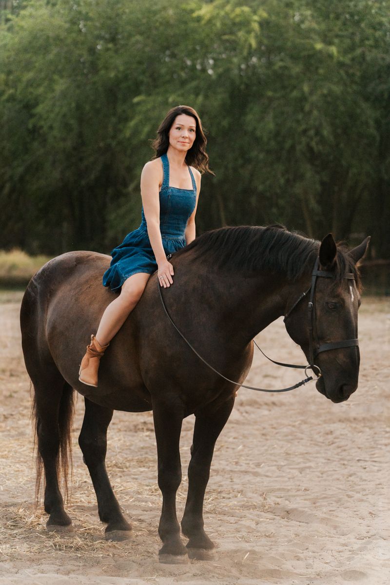 Woman in a blue dress poses with a dark horse in a natural outdoor setting Sydney horse photoshoot hills