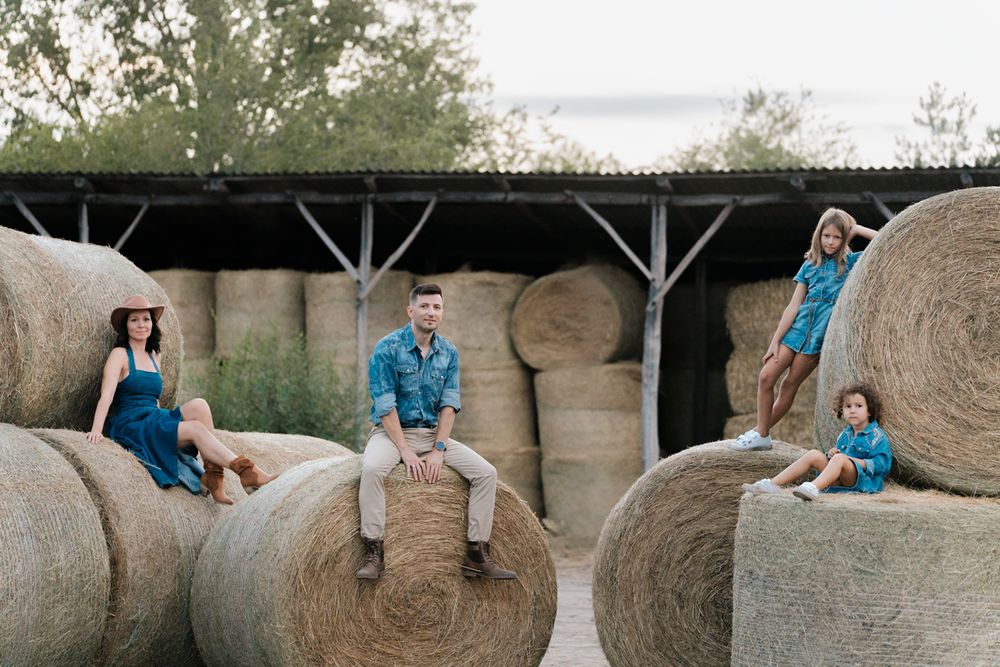 Family sitting on large round hay bales in a rustic outdoor setting during a photo session in Sydney