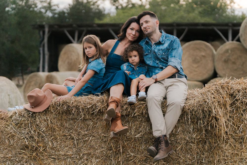Family relaxing together on rustic hay bales in golden outdoor setting during sunset photo session Western Sydney