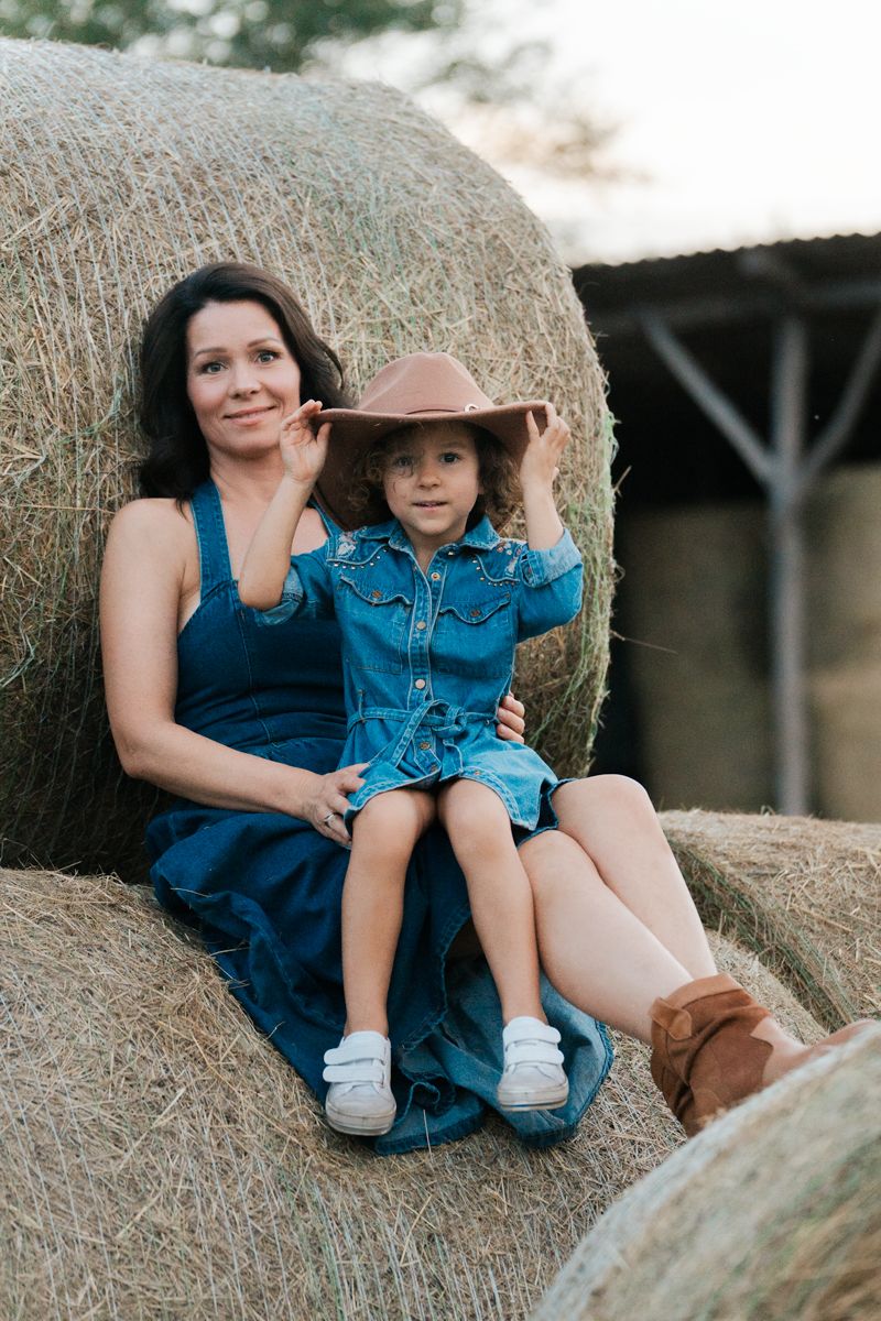 A parent and child wearing blue outfits sit together on hay bales at a rustic outdoor family portrait in Sydney