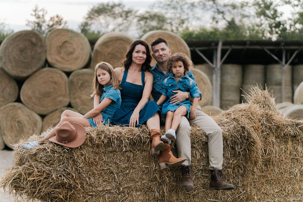 Family sitting together on rustic hay bales in coordinated blue outfits during outdoor photo session in Sydney