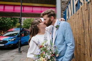 A couple embraces in a garden setting with bamboo fencing and colorful flowers during a wedding celebration.