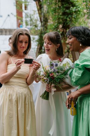 Bridesmaids in cream and mint green dresses hold bouquets while sharing emotional moments.