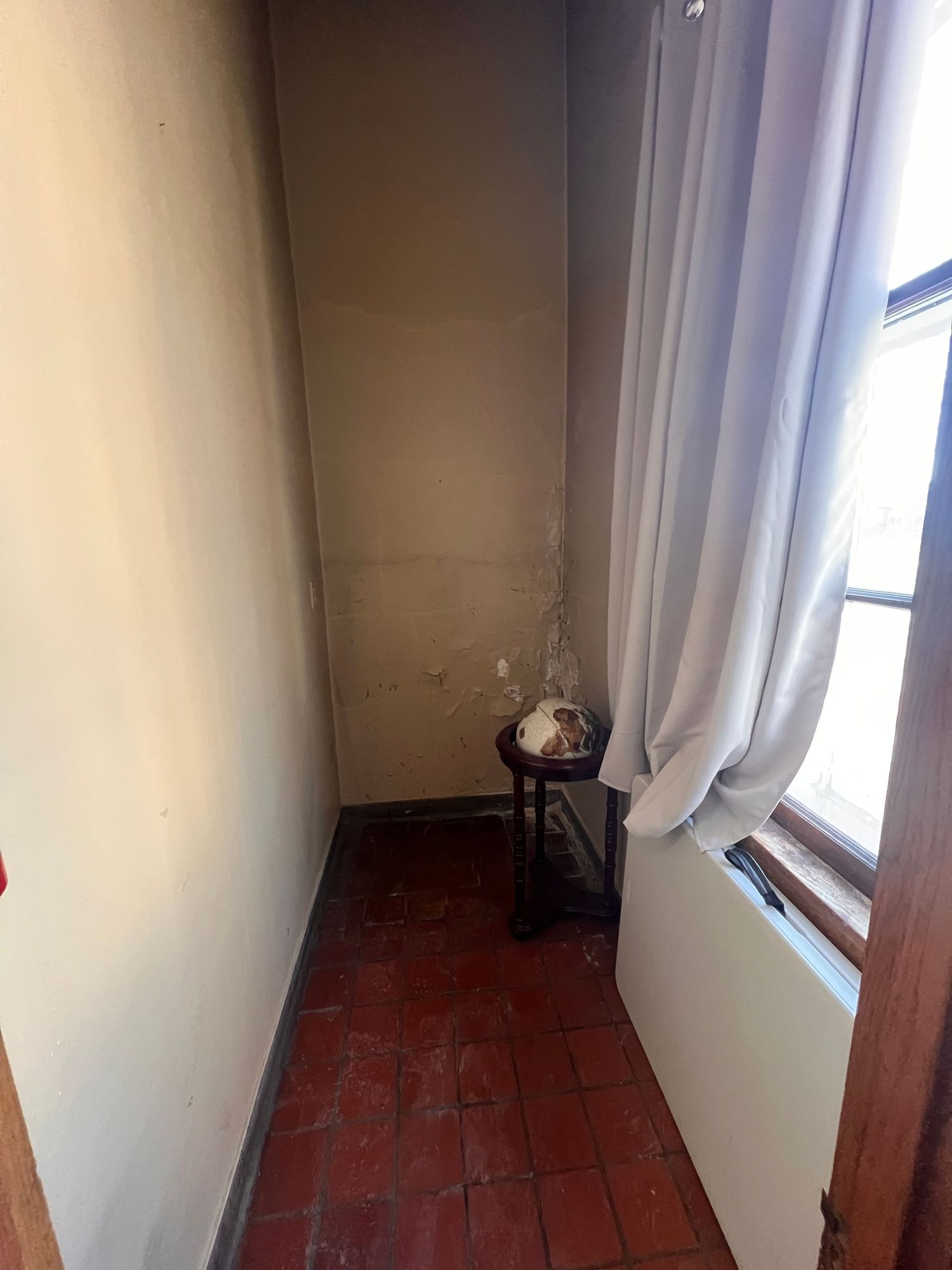 Narrow room with white walls, red tile flooring, and long curtains framing a window.