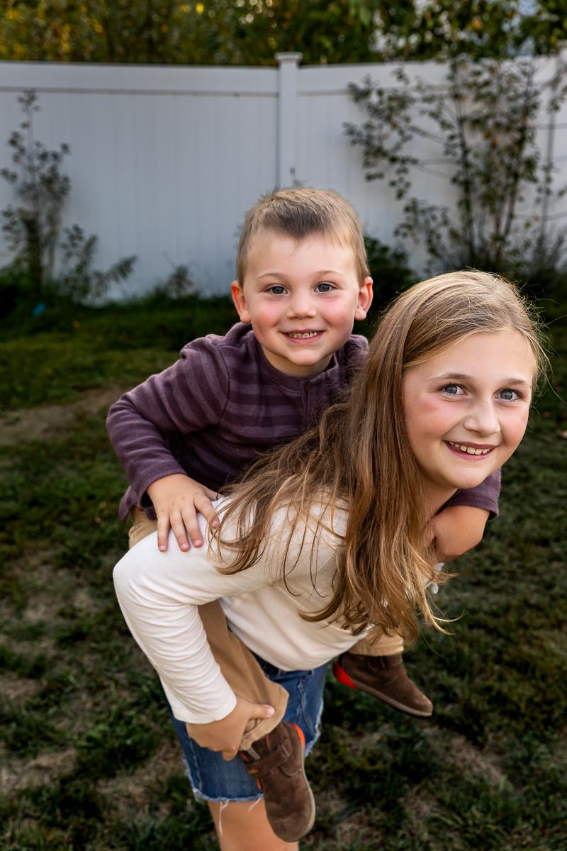 Two young siblings playing together outdoors, with one getting a playful piggyback ride.