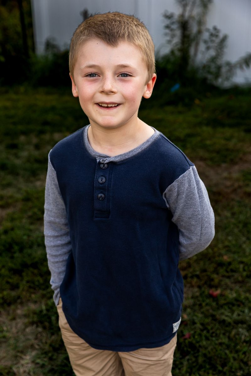 Young child wearing a navy and gray shirt smiles at camera while playing outside.