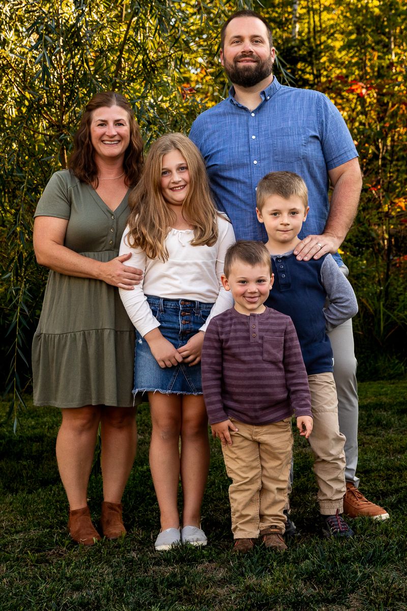 A happy family of five poses together outdoors on an autumn day with golden foliage in the background.
