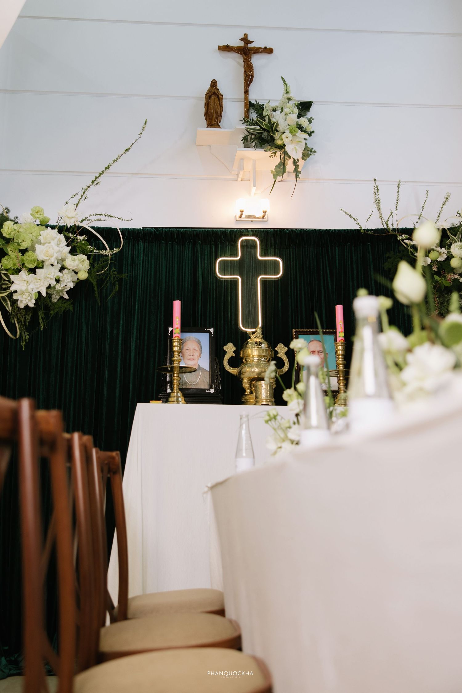 Catholic wedding ceremony altar with glowing cross, candles, and white floral decorations in a chapel.