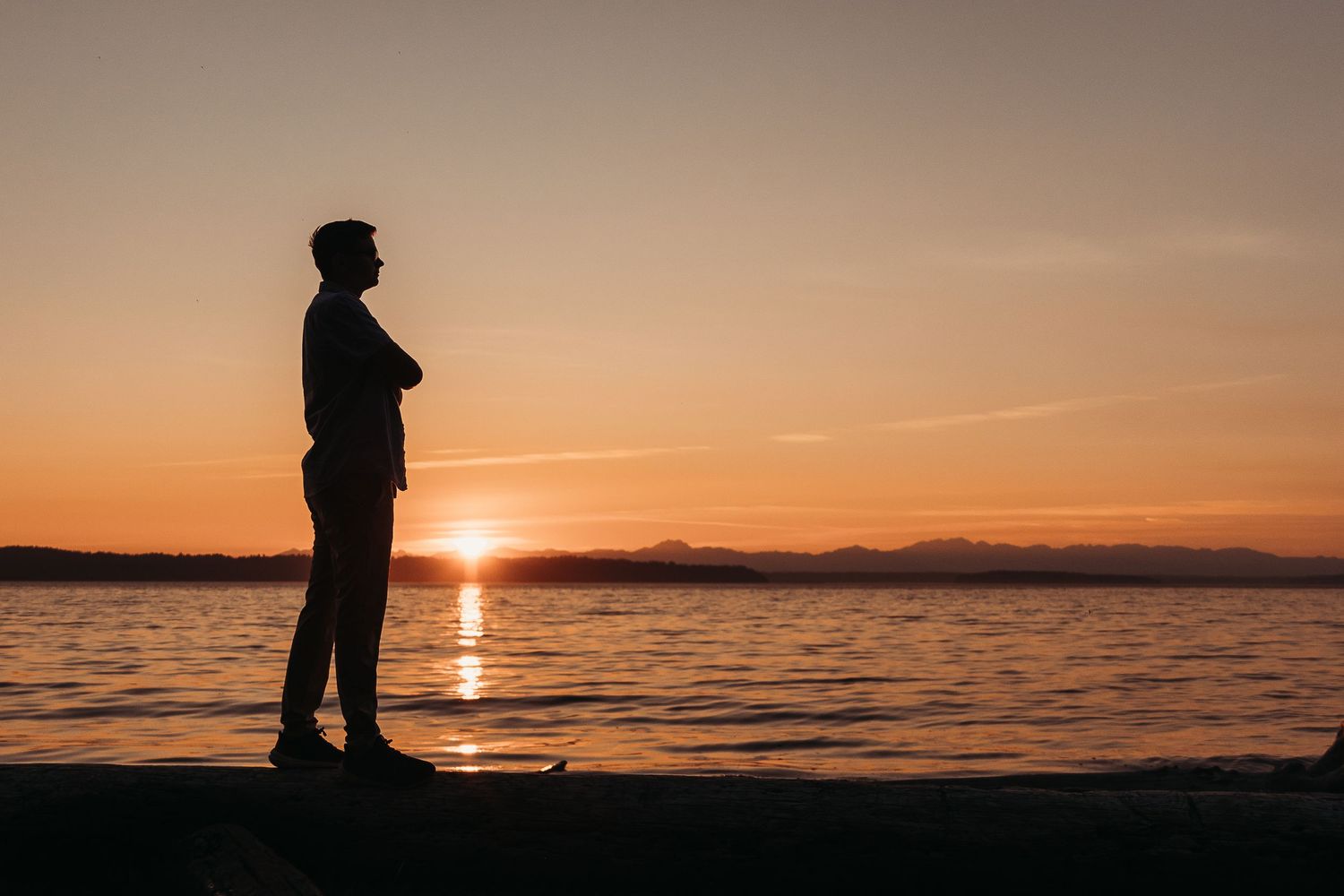 A waterfront scene at sunset shows two figures splashing in the shallow waves along the shoreline.