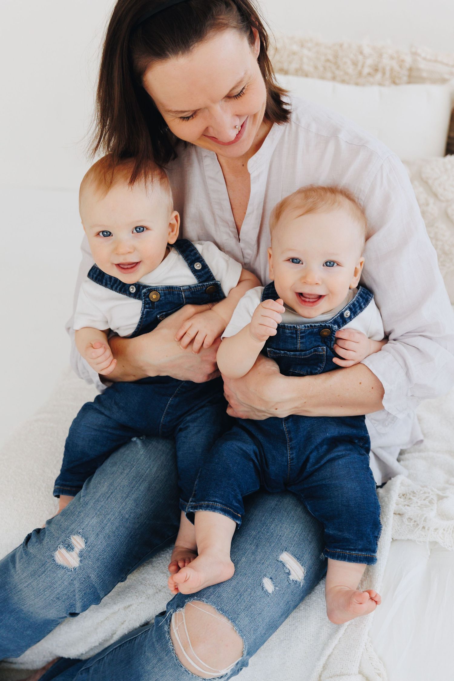 Joyful toddler in blue denim overalls and cream sweater laughs while sitting against white background.