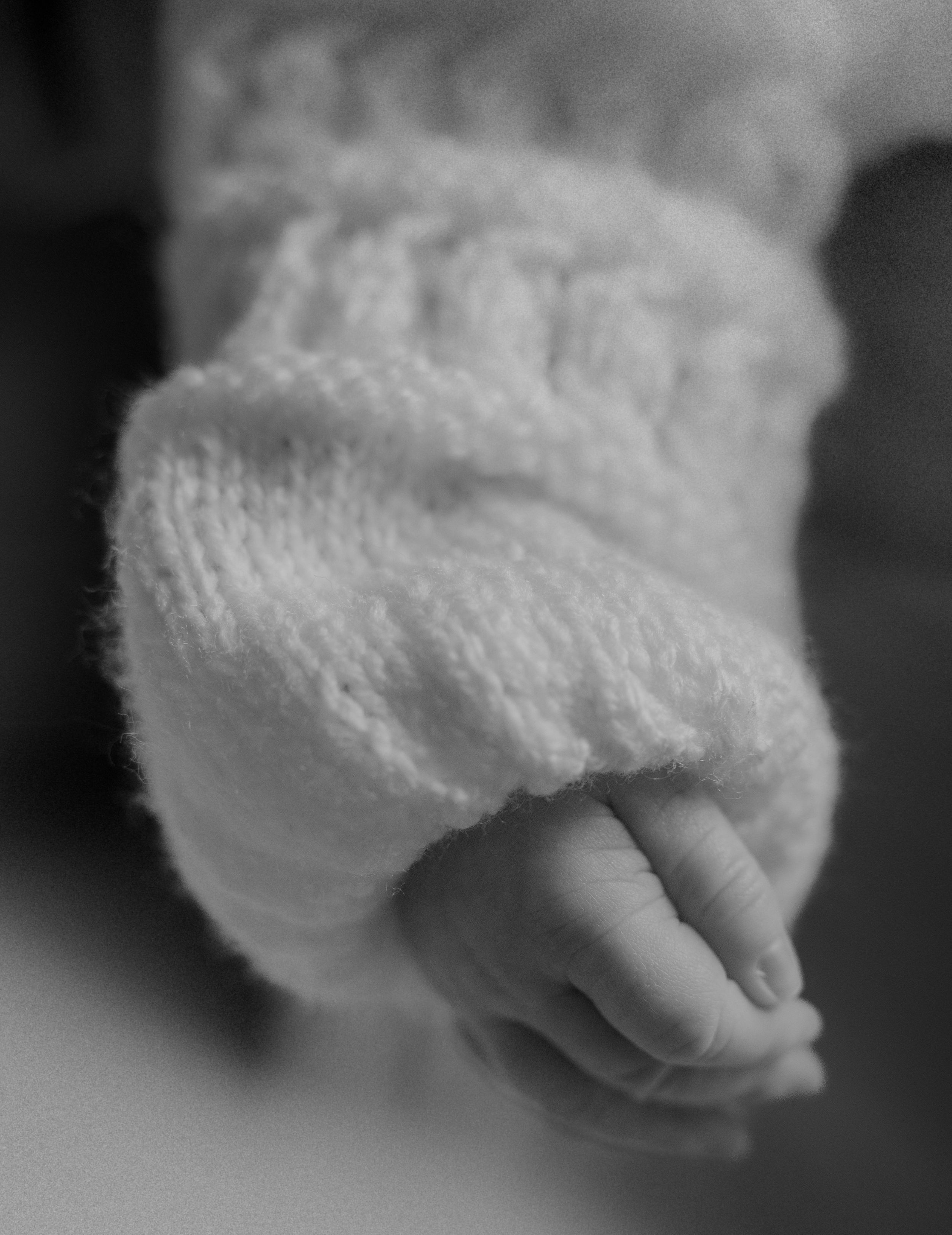 A series of black and white macro shots showing a tiny baby's foot wrapped in soft white fabric.