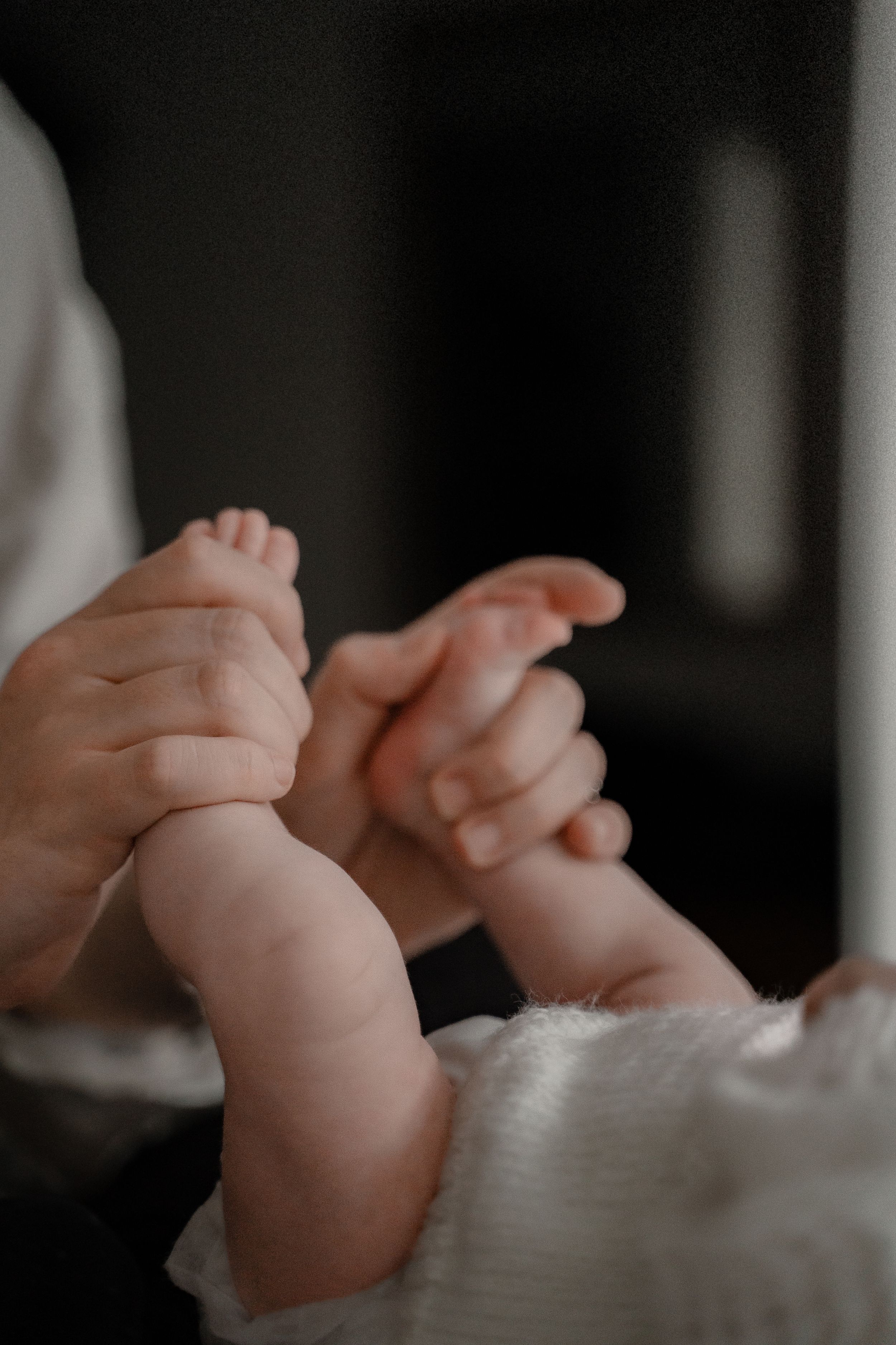 Close-up black and white photo of tiny baby feet against a soft white blanket in dim lighting.
