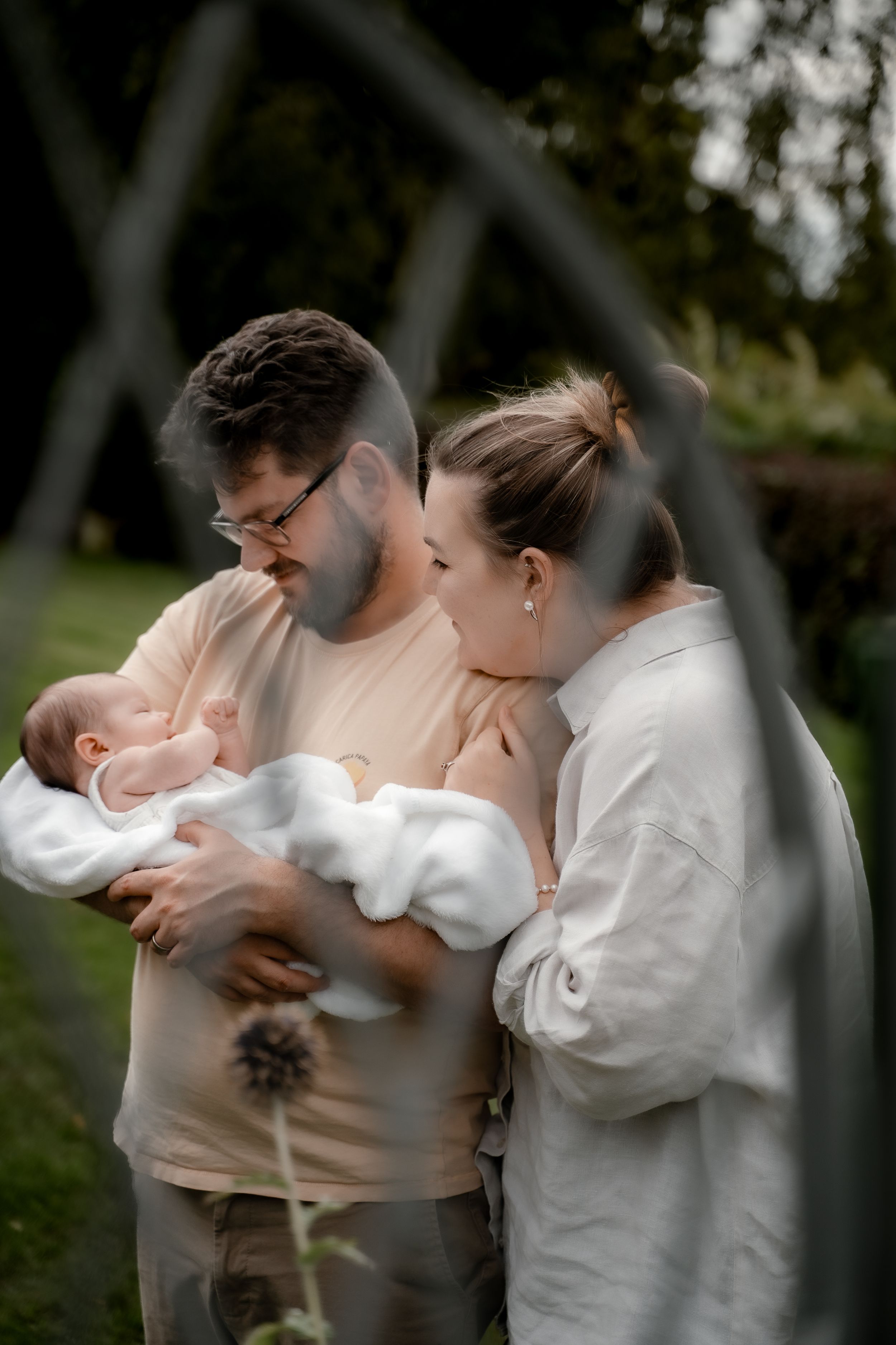 A tender moment captured in motion as a couple embraces their baby in white clothing outdoors.