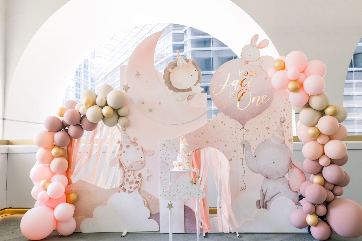 Elegant blush pink and white balloon arch installation with metallic accents decorates an indoor event space.