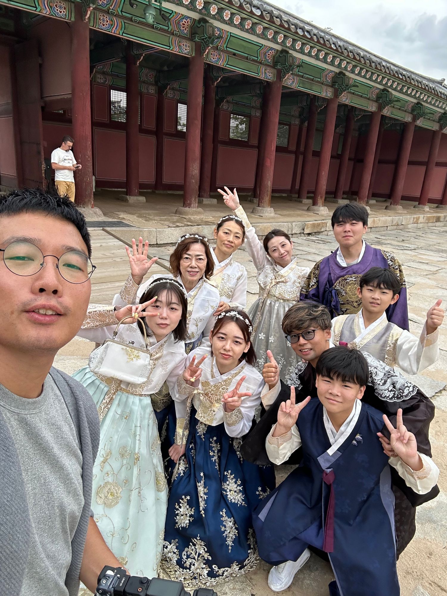 A group poses together in front of traditional Korean palace architecture with ornate roof details and red columns.