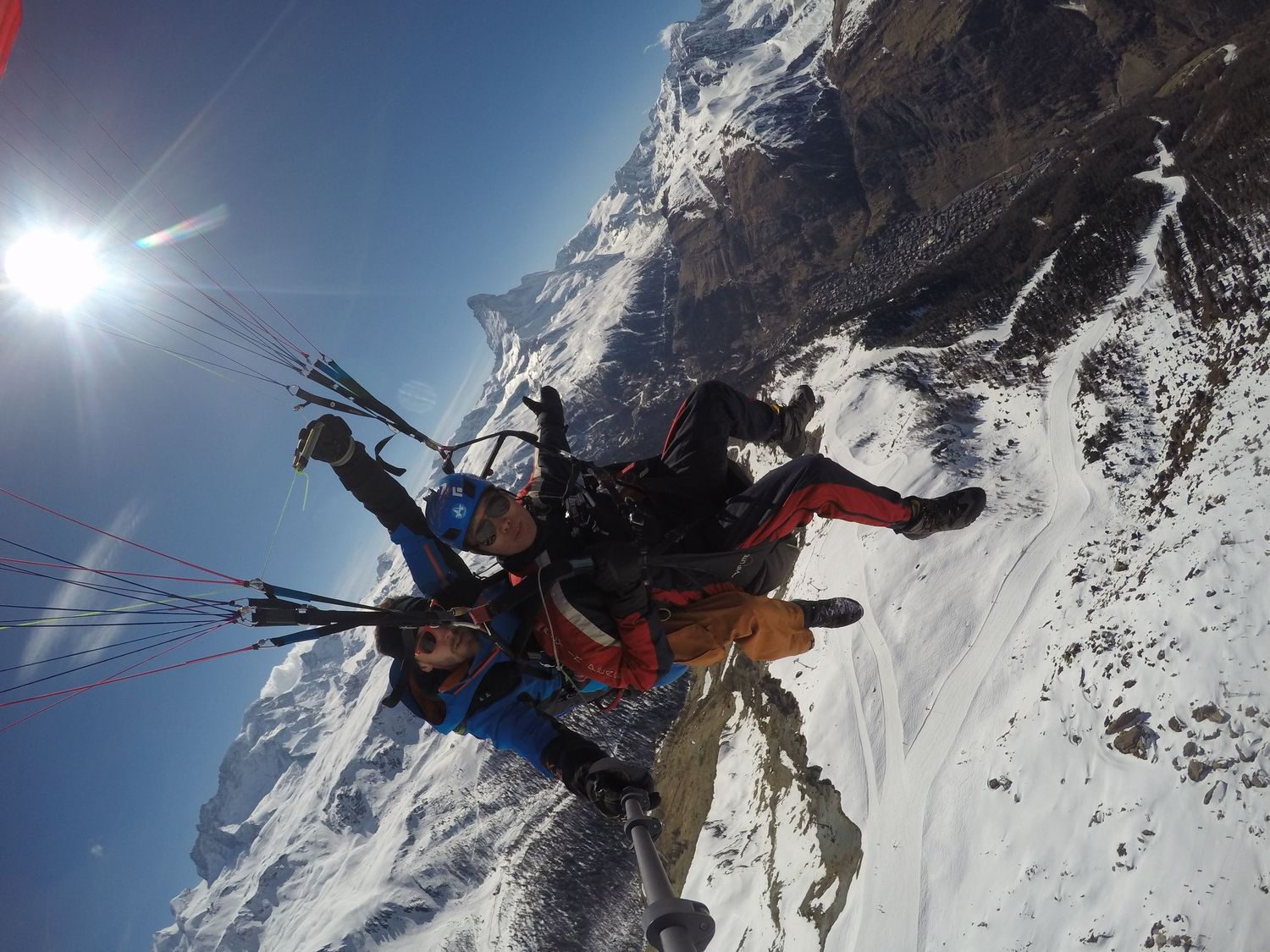 Adventurous skiers descending steep mountain slopes in deep powder snow conditions during a bright sunny day.