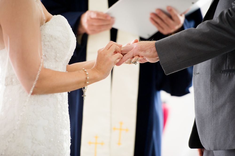 A close up of a bride and groom exchanging rings during their wedding ceremony in a church.