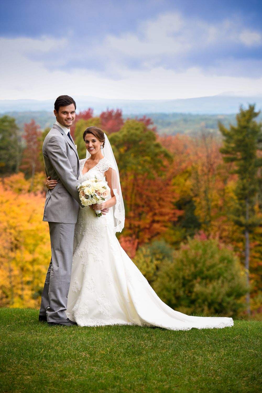 Newlyweds posing together on a hilltop surrounded by vibrant autumn foliage.