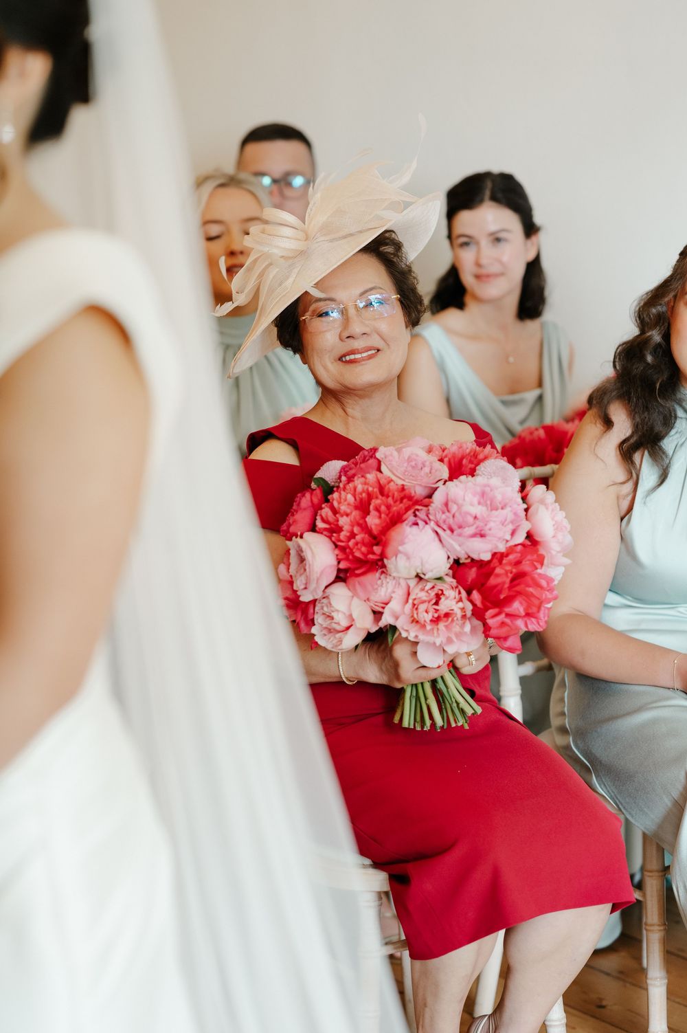 Wedding party members in various colored dresses gather with bright pink and coral bouquets of flowers.