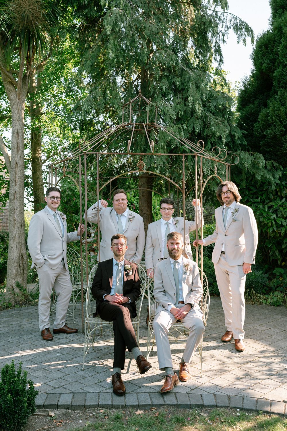 Groomsmen in light gray suits pose playfully on outdoor swings in a garden setting.